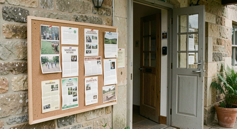 A community noticeboard with pinned cards and leaflets in a village hall entrance.